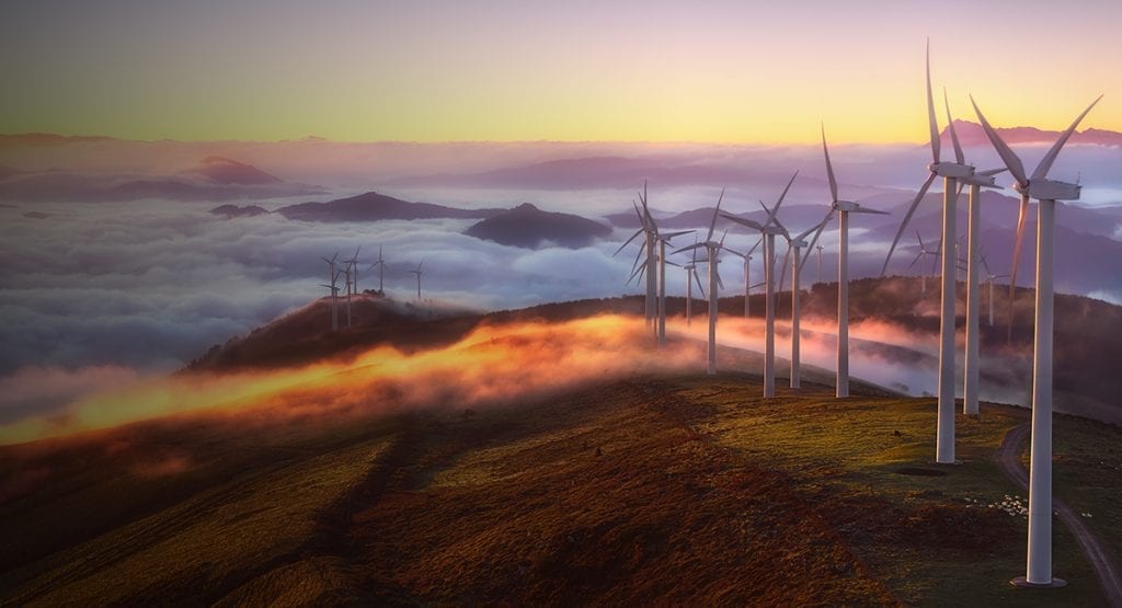 Turbines glow at sunrise in the morning mist on a hilltop wind farm